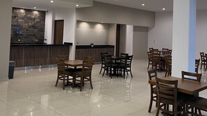 Un comedor amplio con varias mesas y sillas de madera, una lámpara moderna y una pared de acento de piedra.
