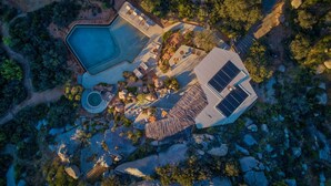 Vista aérea de una propiedad con piscina, un porche cubierto y un edificio equipado con paneles solares.