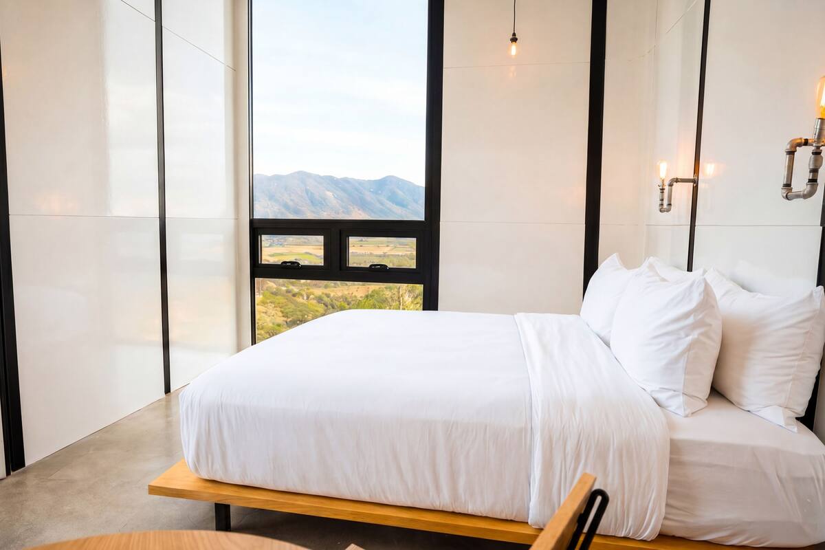 Un dormitorio con una cama, vistas a las montañas y una ventana con un panorama.