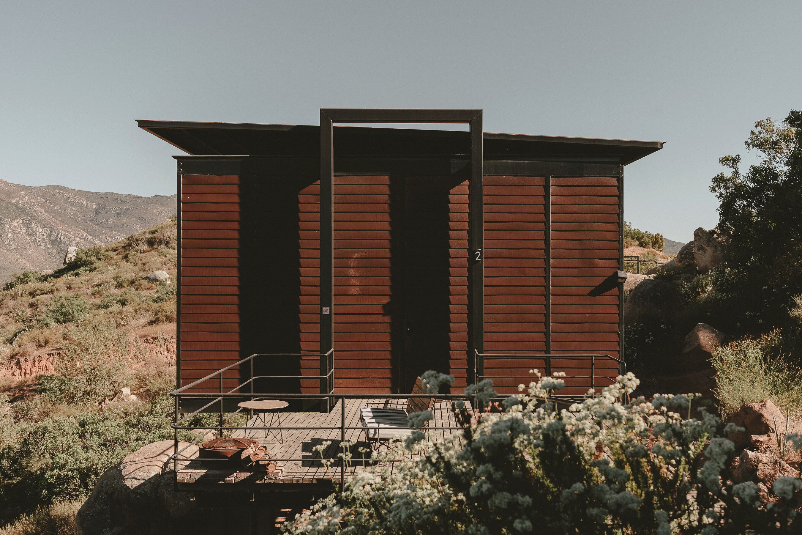 Un edificio pequeño de una sola planta con techo plano, una puerta y un espacio al aire libre con mesas y sillas.