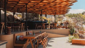Un espacio al aire libre con mobiliario de madera y una barra, rodeado de formaciones rocosas naturales y vegetación.