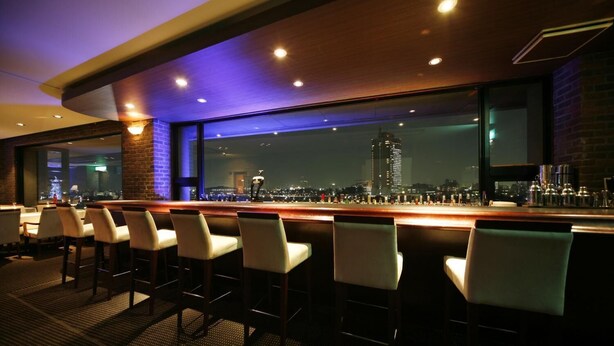 Un área de bar con asientos y vistas a un paisaje urbano nocturno.