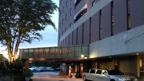 Entrada de un hotel con un cartel que dice "HOTEL SANDERSON", un camino pavimentado y un coche estacionado.