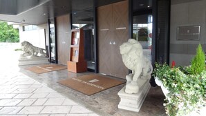 Una entrada de hotel moderna con una estatua de león, felpudo y un mostrador de recepción.