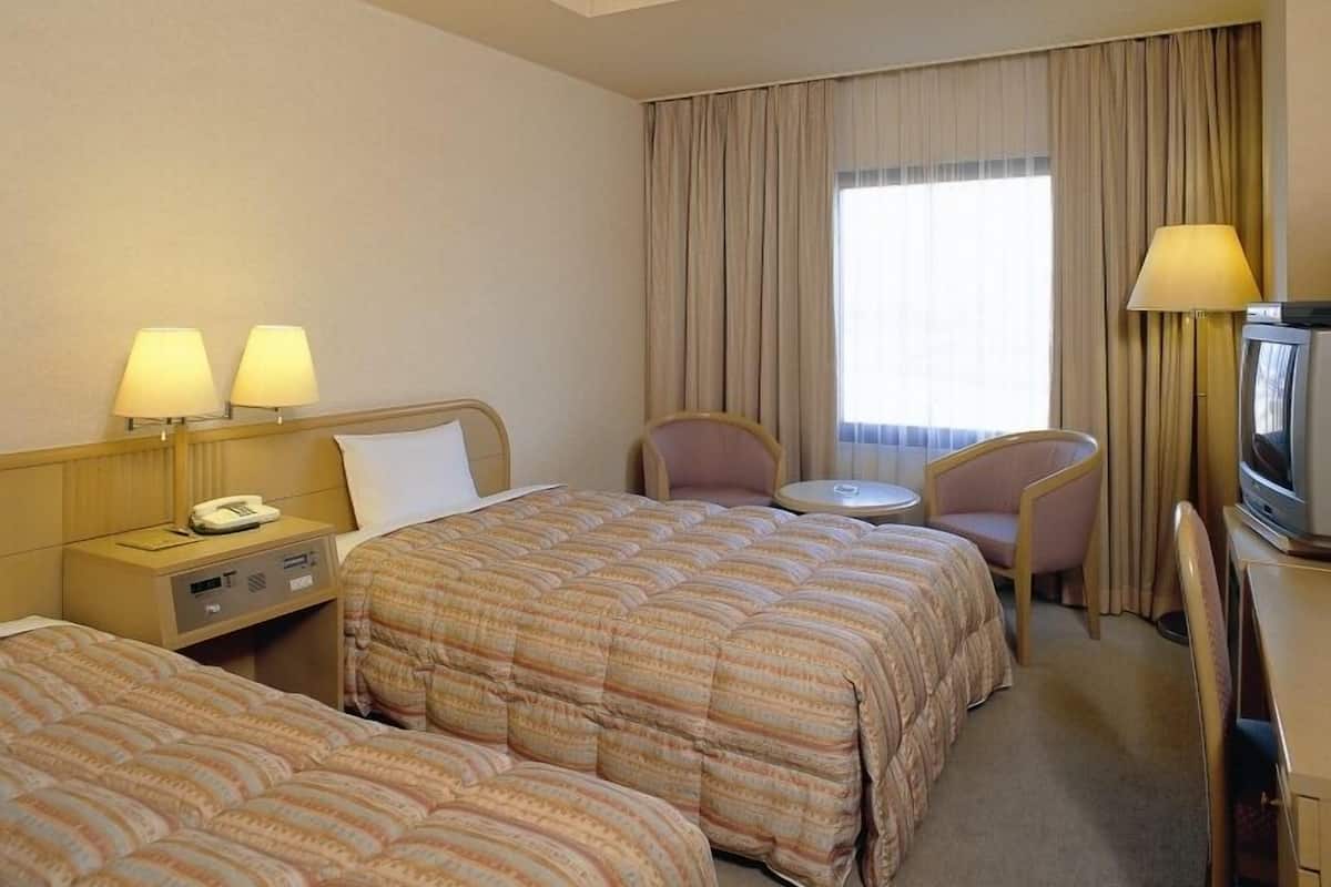 A hotel room with two beds, a desk with a television, a chair, and a small table.