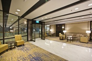 Eine moderne Hotelhalle mit Glaswänden, einem Marmorboden und einer Sitzecke mit Sofas und Sesseln.