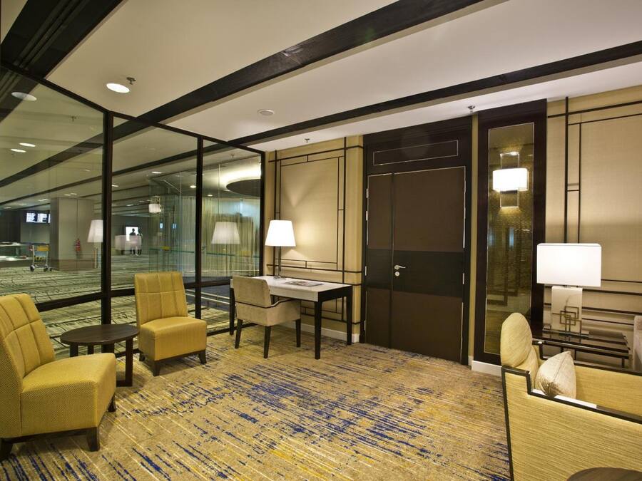 A hotel lobby with a seating area, a reception desk, and a large glass wall offering a view of the lobby area.
