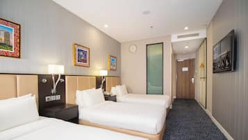 A hotel room with three beds, a clock, and a television screen displaying a welcome message.