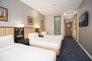 Ein Hotelzimmer mit drei Betten, einer Uhr und einem Fernseher, der eine Willkommensnachricht zeigt.