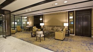 Un moderno vestíbulo de hotel con piso de mármol, un conjunto de sofás, sillones, una mesa de centro y un televisor grande montado en la pared.