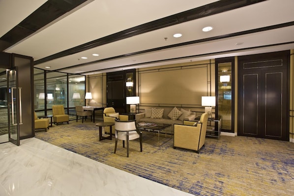 A modern hotel lobby with a marble floor, a sofa set, armchairs, a coffee table, and a large wall-mounted TV. -  Changi Transit Hotel Terminal 3 (Singapore)