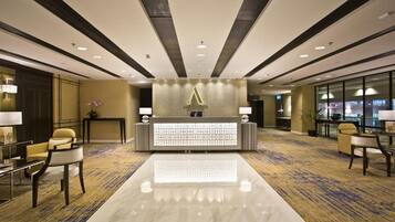 Zona de recepción de un hotel con diseño moderno, que incluye un mostrador de recepción, un área de estar y piso alfombrado.
