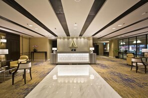 Zona de recepción de un hotel con diseño moderno, que incluye un mostrador de recepción, un área de estar y piso alfombrado.