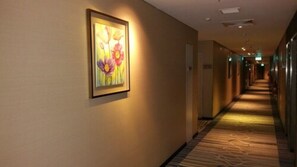 A hotel hallway with a framed floral artwork on the wall, carpeted flooring, and a long corridor with doors on one side. -  Changi Transit Hotel Terminal 3 (Singapore)