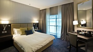 Habitación de hotel con una cama grande, un escritorio, una silla, un espejo y una ventana con cortinas.