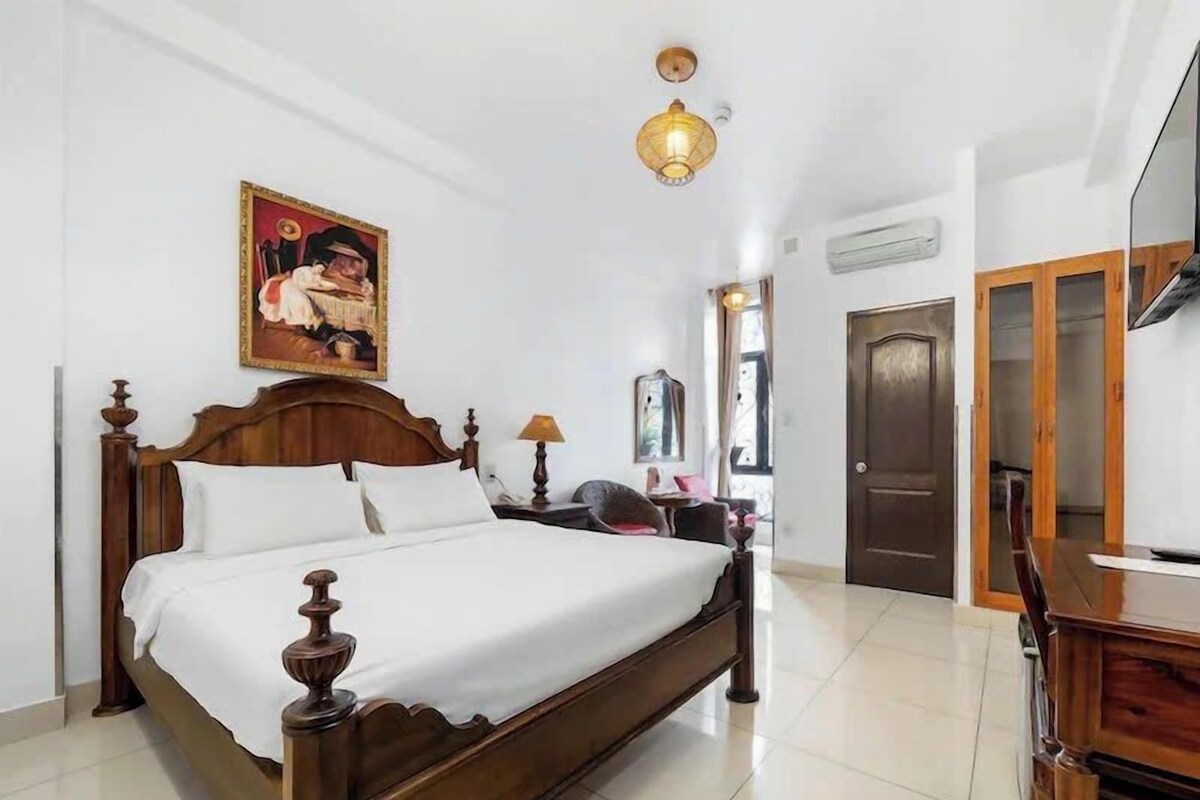 A bedroom with a wooden bed, a painting on the wall, a lamp, and a door.