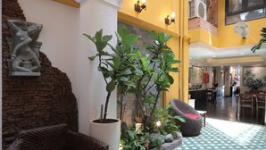 Recepció amb paret de maó, una gran planta en test, mobles de vímet i un paviment amb dibuixos.