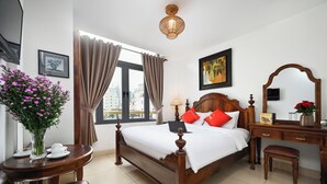 Habitació d'hotel ordenada amb un llit de fusta, escriptori, cadira, taula petita amb un ram de flors i una finestra amb cortines.