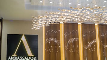 A hotel reception area with a prominent 'Ambassador Transit Hotel' sign, modern lighting fixtures, and a wooden reception desk.