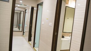 Un pasillo con varias puertas, cada una que da acceso a un baño con espejo y lavamanos.
