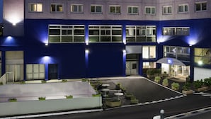 Un hôtel à plusieurs étages, dont la façade est ornée d’une grande enseigne « HÔTEL », se distinguant par son design moderne, avec des fenêtres régulièrement espacées et un toit plat.