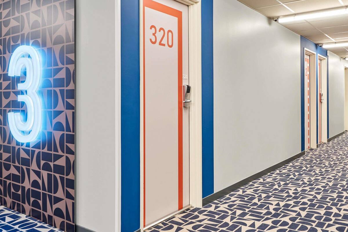 Un couloir d’hôtel avec un mur orné d’un motif géométrique, une porte portant l’inscription « 320 », et un sol présentant un motif similaire.