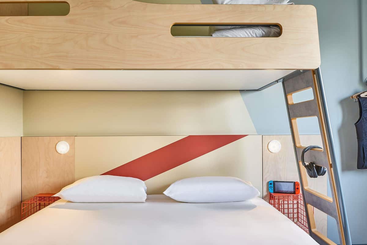 Un lit superposé avec une tête de lit en bois, une échelle et une petite table de chevet avec un casque audio.