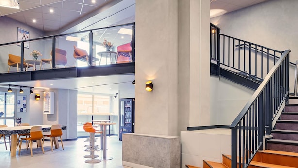 Un hall d’entrée spacieux avec un escalier, un comptoir d’accueil et un espace détente comprenant des tables et des chaises.