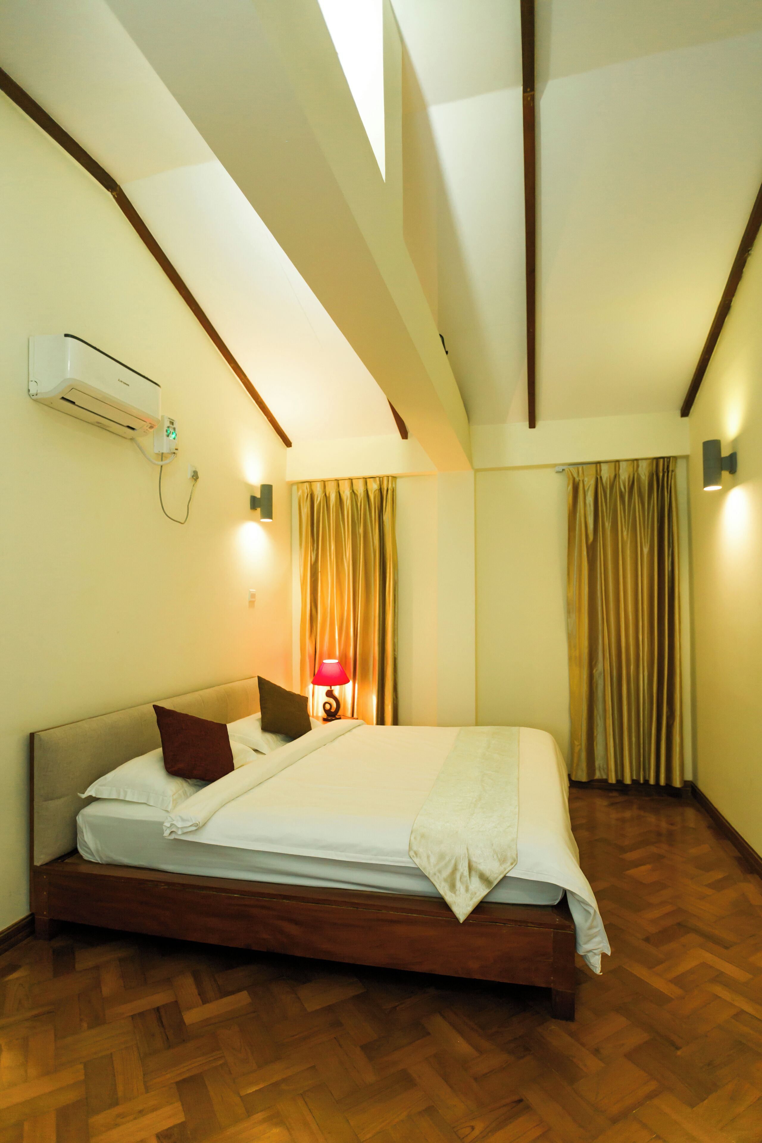 A bedroom with a wooden bed, a nightstand with a lamp, and a window with curtains.