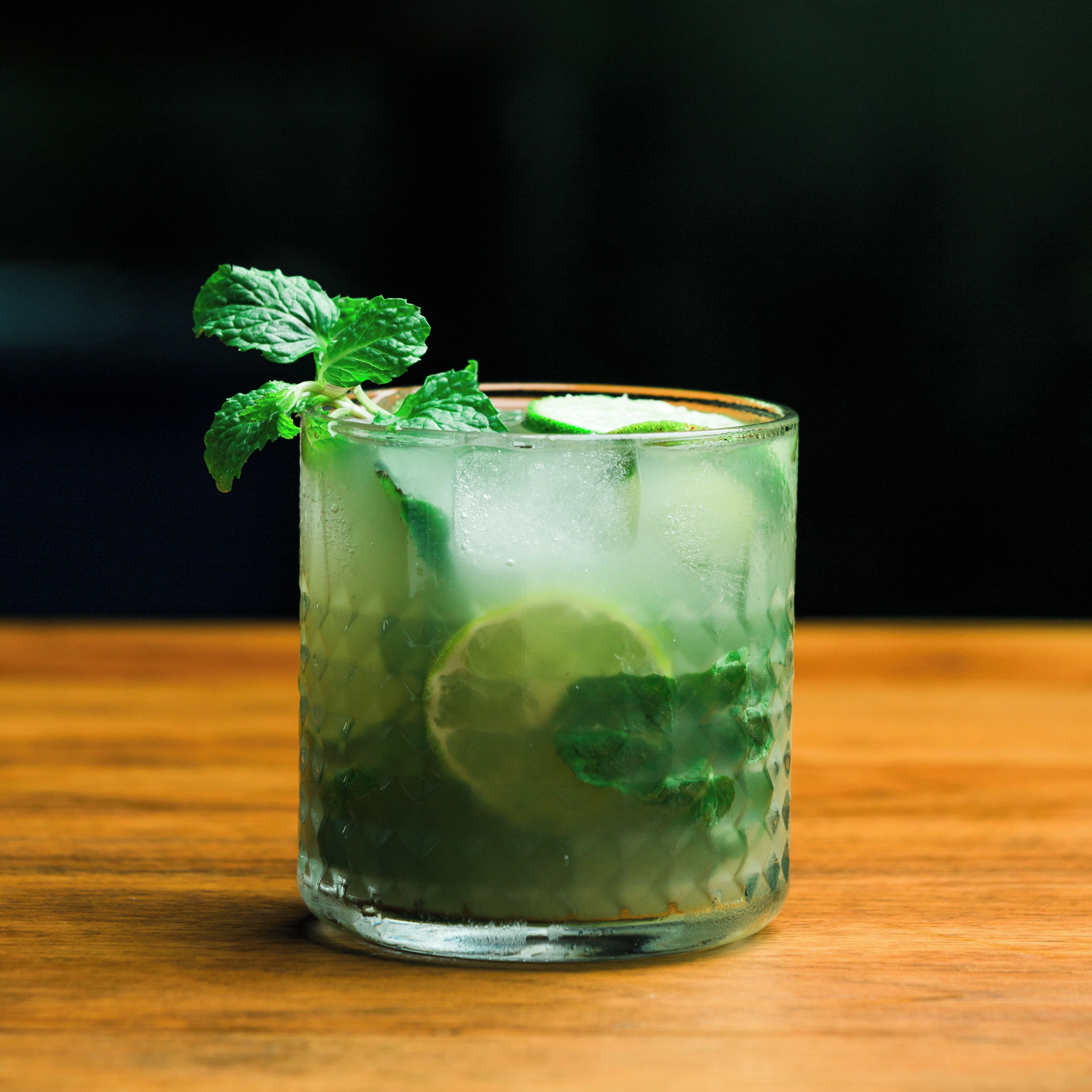 Un vaso de mojito con hojas de menta y lima sobre una superficie de madera.