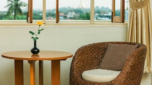 Una silla de mimbre con un cojín y una pequeña mesa de madera con un florero que contiene una sola flor amarilla.