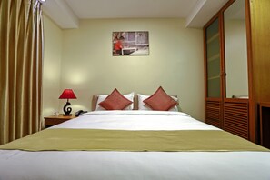 A hotel room with a bed, a nightstand with a lamp, a telephone, and a painting on the wall. - Ambassador Hill (Yangon)