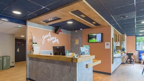 A reception desk with a neon sign, a computer, and a TV screen. - B&B HOTEL Châteauroux A20 L'Occitane (Deols)