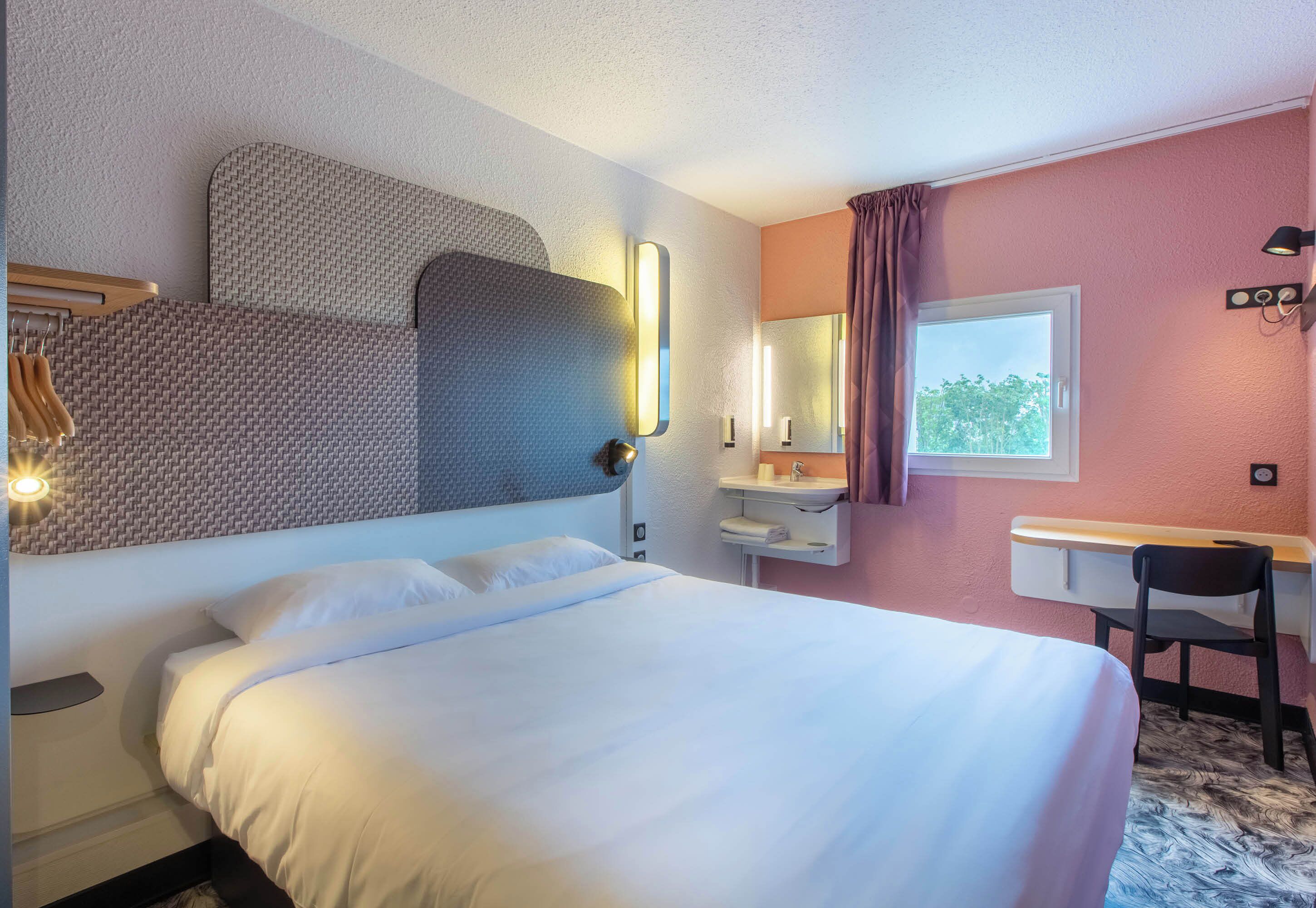 Habitación de hotel con cama, escritorio, silla, espejo y ventana.