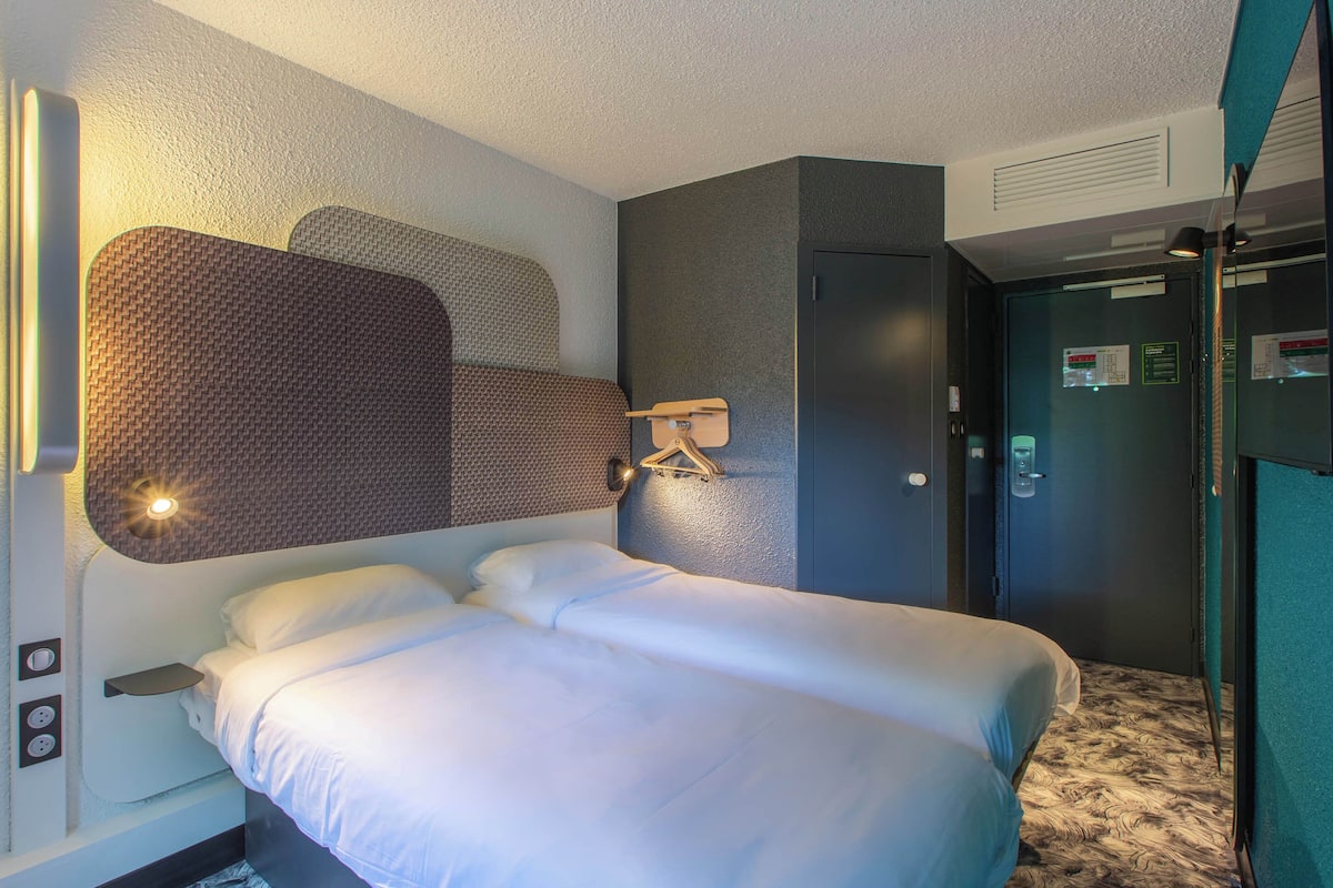 Quarto de hotel com uma cama grande, um guarda-roupa e um candeeiro fixado na parede.