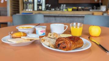 Un desayuno con cruasanes, pan, una taza de café, un vaso de zumo de naranja y un limón sobre una mesa.