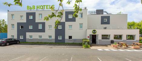 A B&B hotel with a modern design, featuring a parking lot and outdoor seating area.