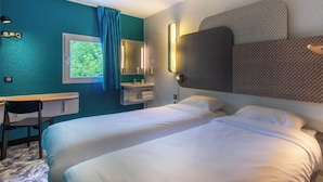 A hotel room with two beds, a desk, a chair, a window with curtains, and a wall-mounted mirror. - B&B HOTEL Châteauroux A20 L'Occitane (Deols)