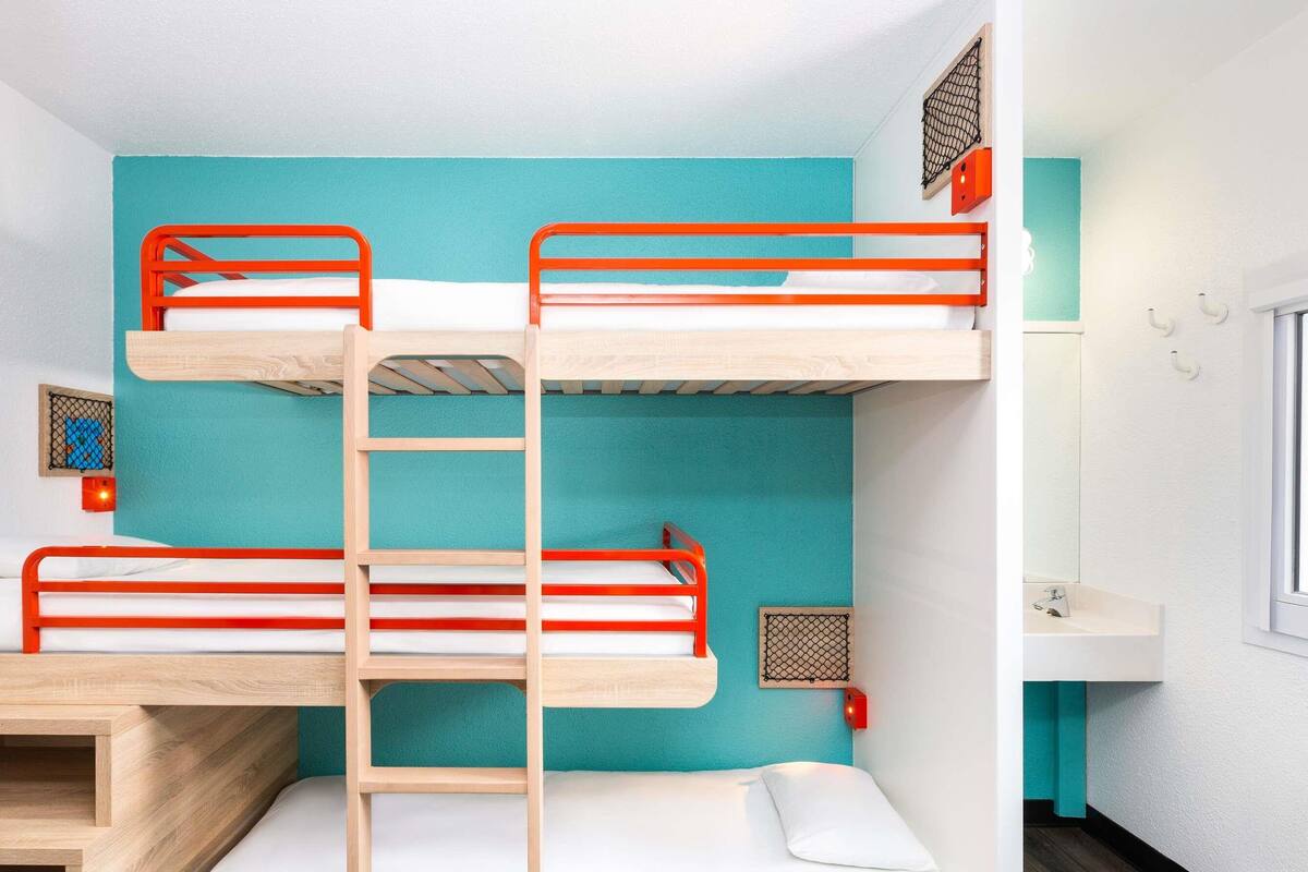 A bunk bed room with a ladder, a small shelf, and a window.