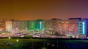 A multi-story hotel with a green-lit facade, a parking lot, and a river in the background. - hotelF1 Roissy CDG (Roissy-en-France)