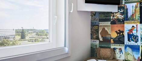 A room with a large window, a flat-screen TV mounted on the wall, a table with a book, and a chair.