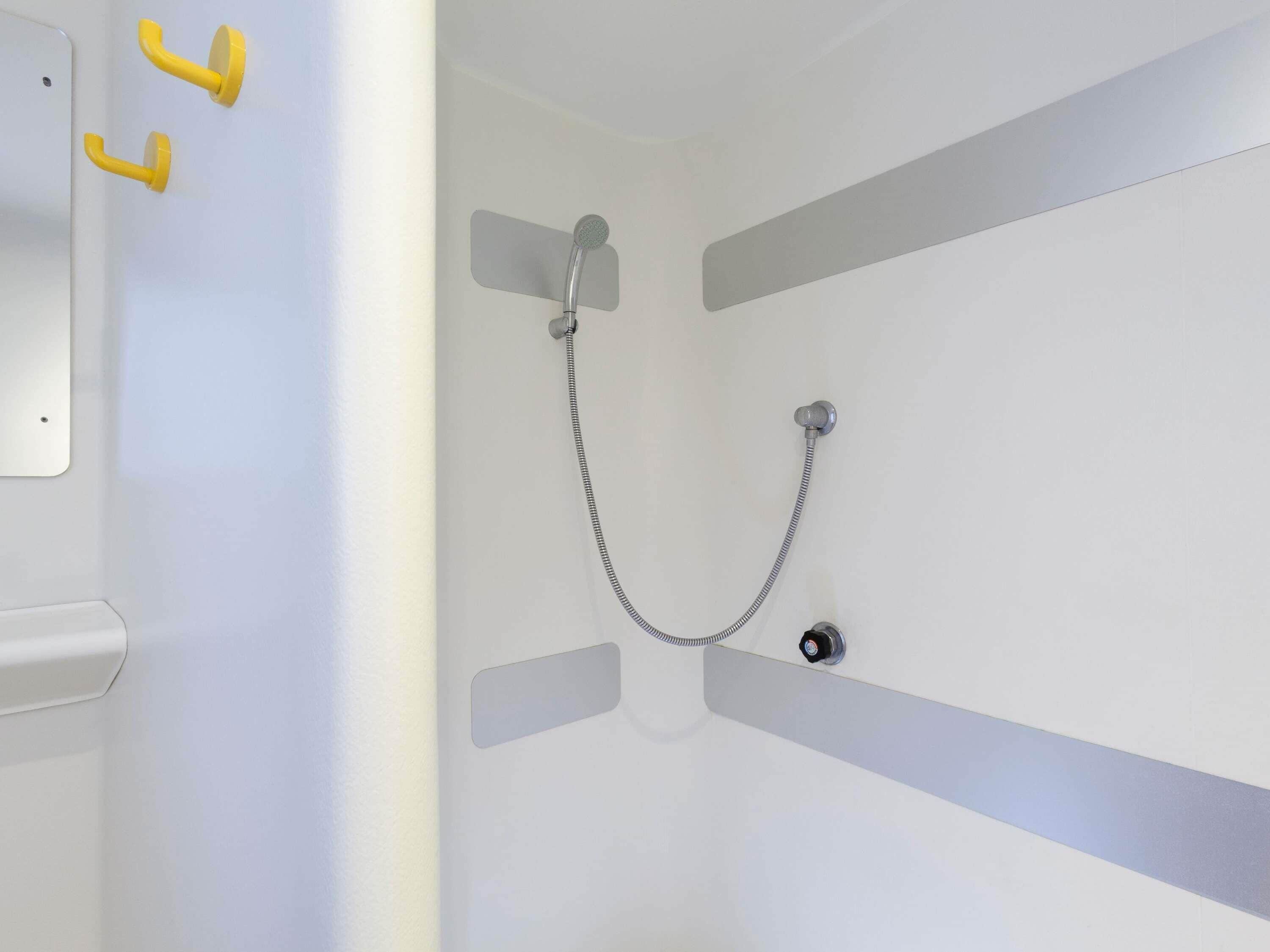 Une douche équipée d’un pommeau de douche à main et d’un robinet de contrôle fixé au mur.