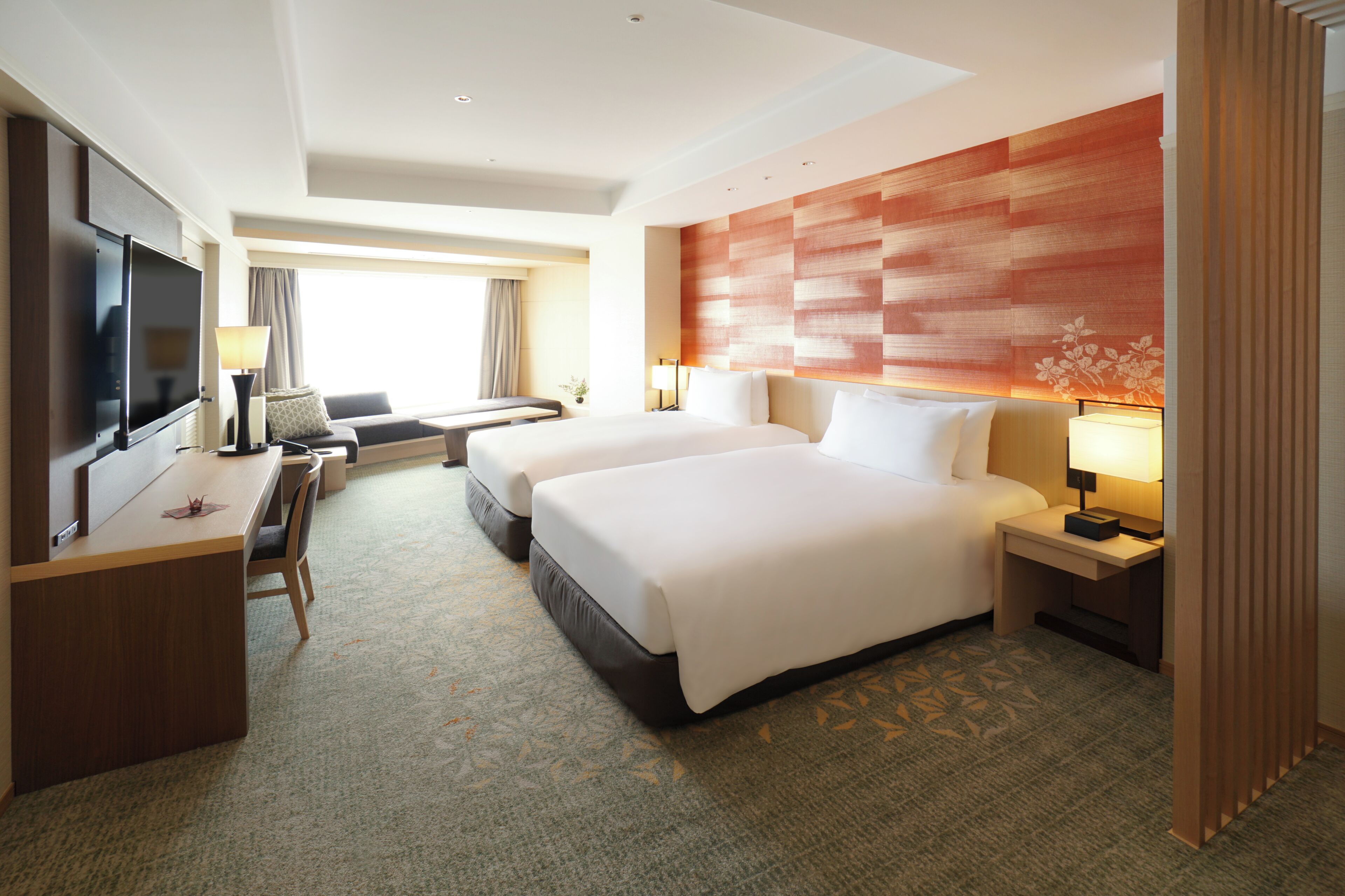 A hotel room with two beds, a desk, a TV, and a large window.