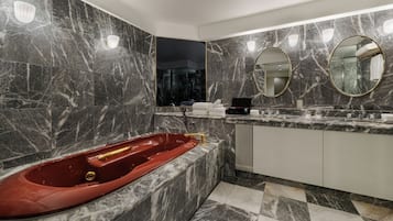 Un baño moderno con suelo de mármol, una bañera de hidromasaje roja, un espejo grande y una ducha con mampara de vidrio.