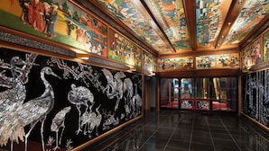 A room with traditional artwork on the walls and ceiling, a polished floor, and a view of a traditional building outside.