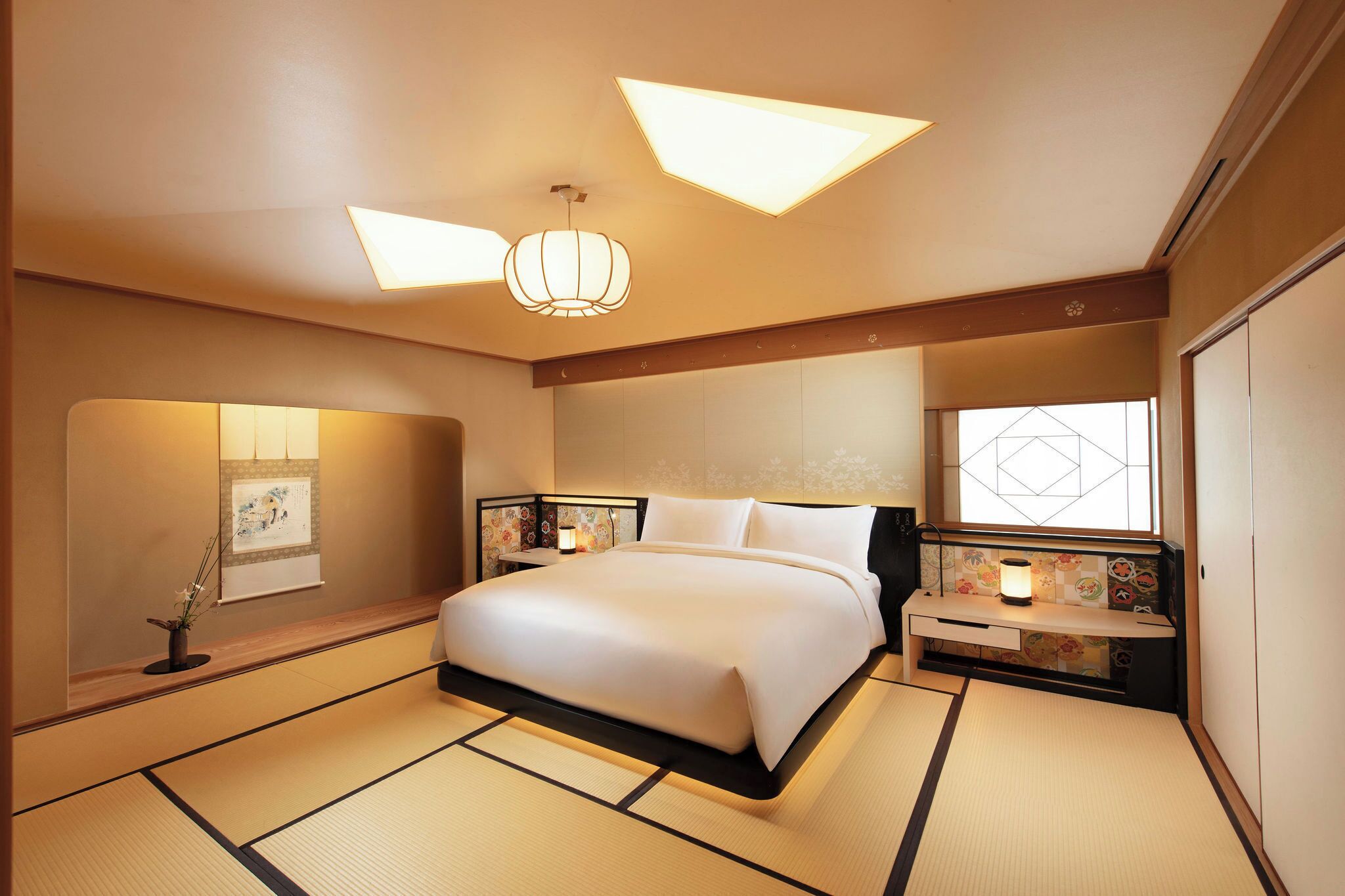 A hotel room with a large bed, bedside tables with lamps, a wall-mounted artwork, and tatami flooring.
