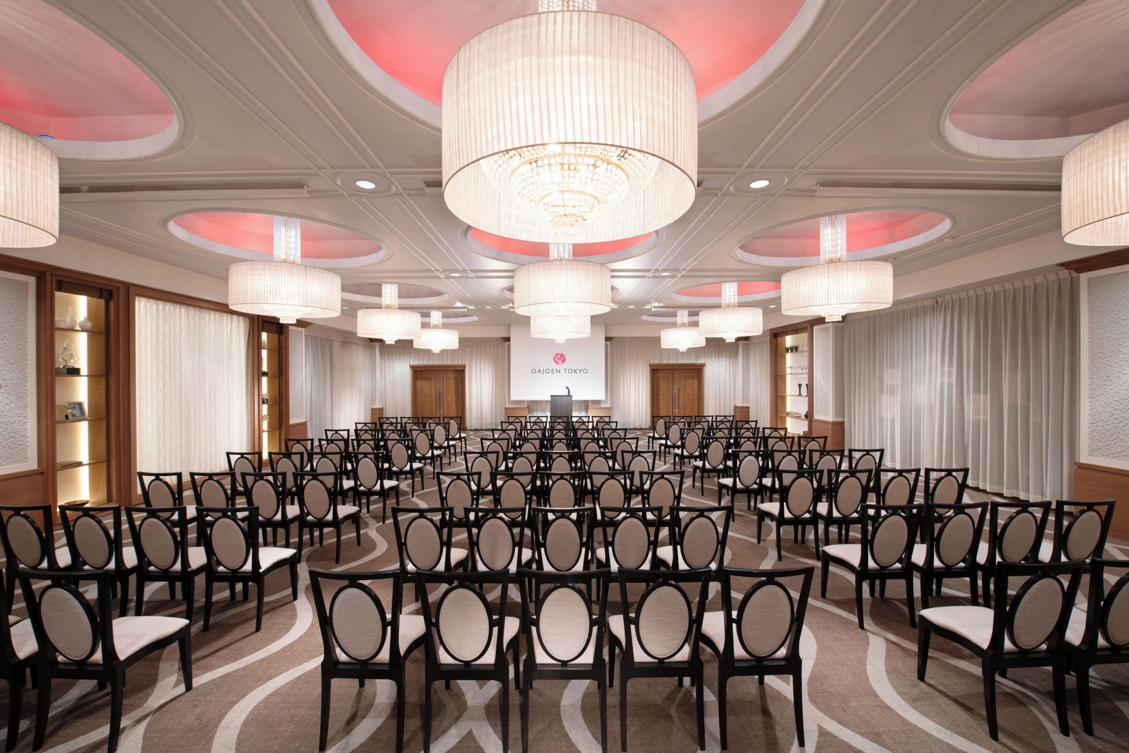 A conference room with rows of chairs, a large chandelier, and a podium at the front.