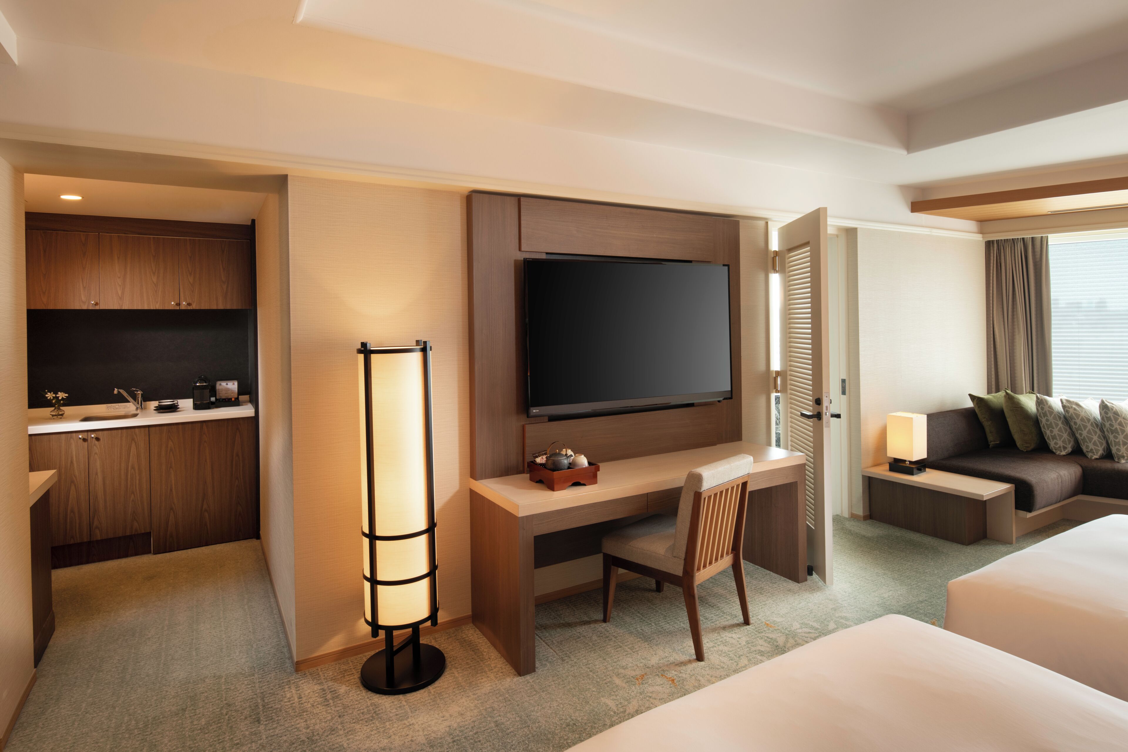 A hotel room with a flat-screen TV, a desk, a chair, a sofa, and a bed.