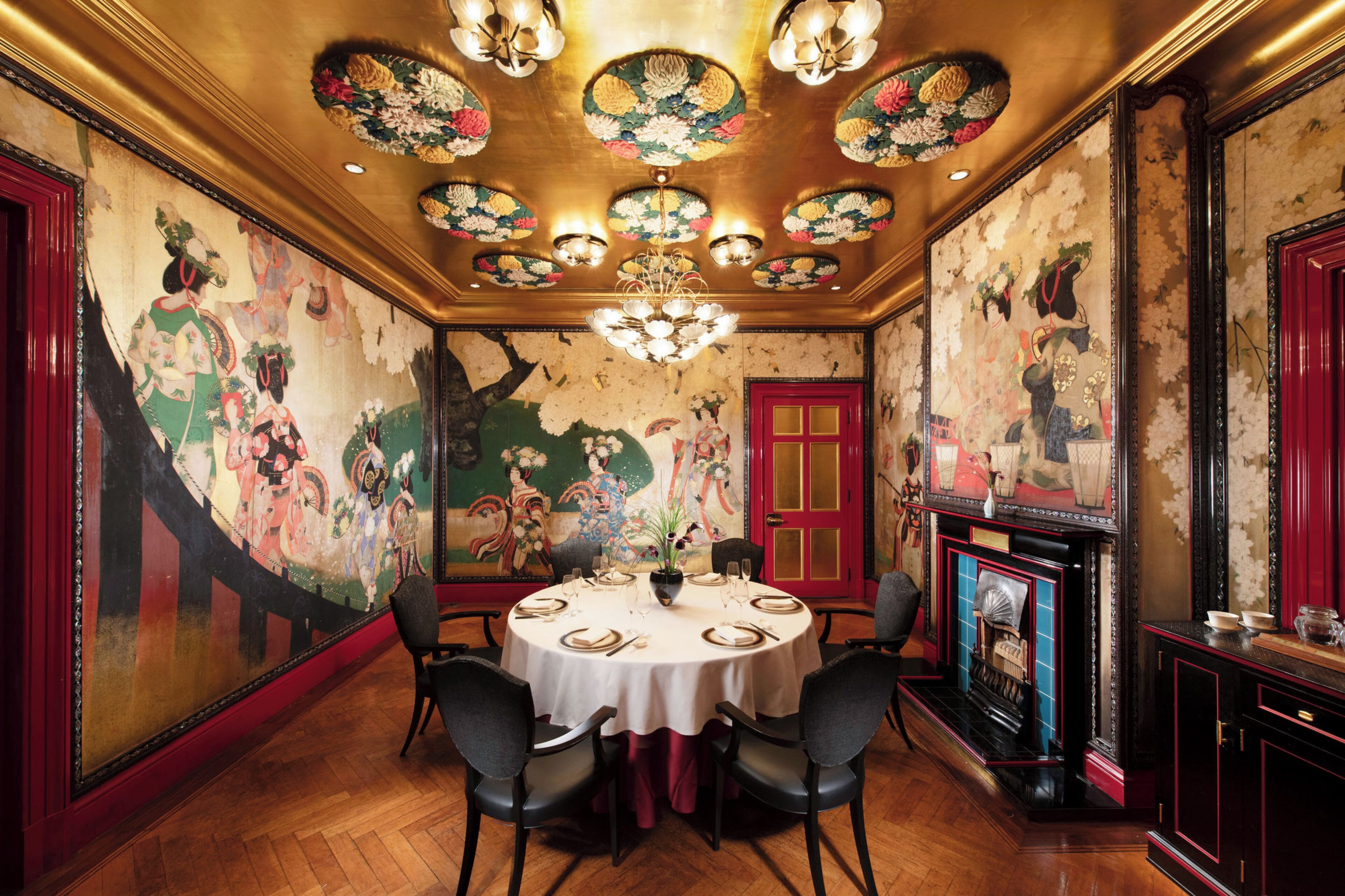 A dining room with a round table, chairs, a chandelier, and a red door.