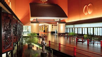 Un hall amplio con diseño arquitectónico asiático tradicional, que presenta una estatua central, una barandilla roja y un gran ventanal con vistas al interior.
